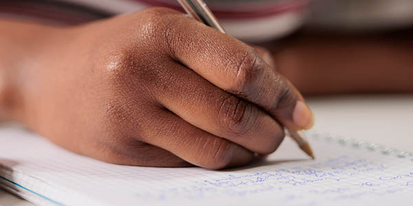 African american woman hand writing with pen in notepad at desk closeup. Student taking notes in planner close view, studying, preparing for exam, doing homework in notebook