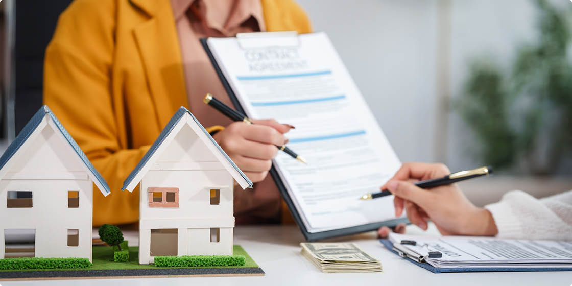Asian businesswoman discusses home purchase contracts with clients at her desk, focusing on loans, mortgages, and other financial aspects of real estate transactions.