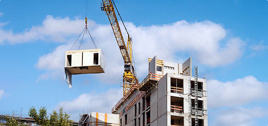 Crane lifting a wooden building module to its position in the structure. Construction site of an office building in Berlin. The new structure will be built in modular timber construction.
