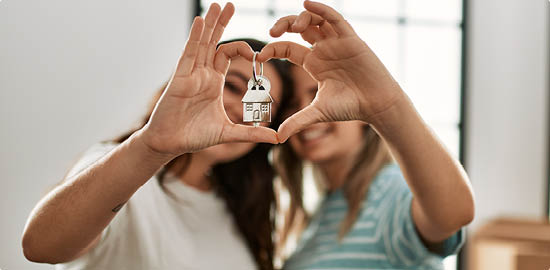 Young couple doing heart symbol with fingers and holding key of new home.